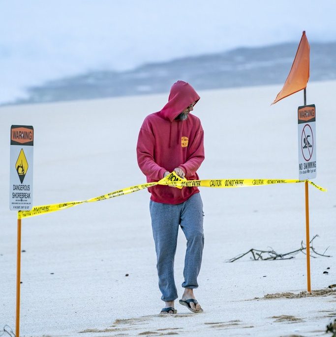 Lifeguard in hoodie putting up caution tape on beach